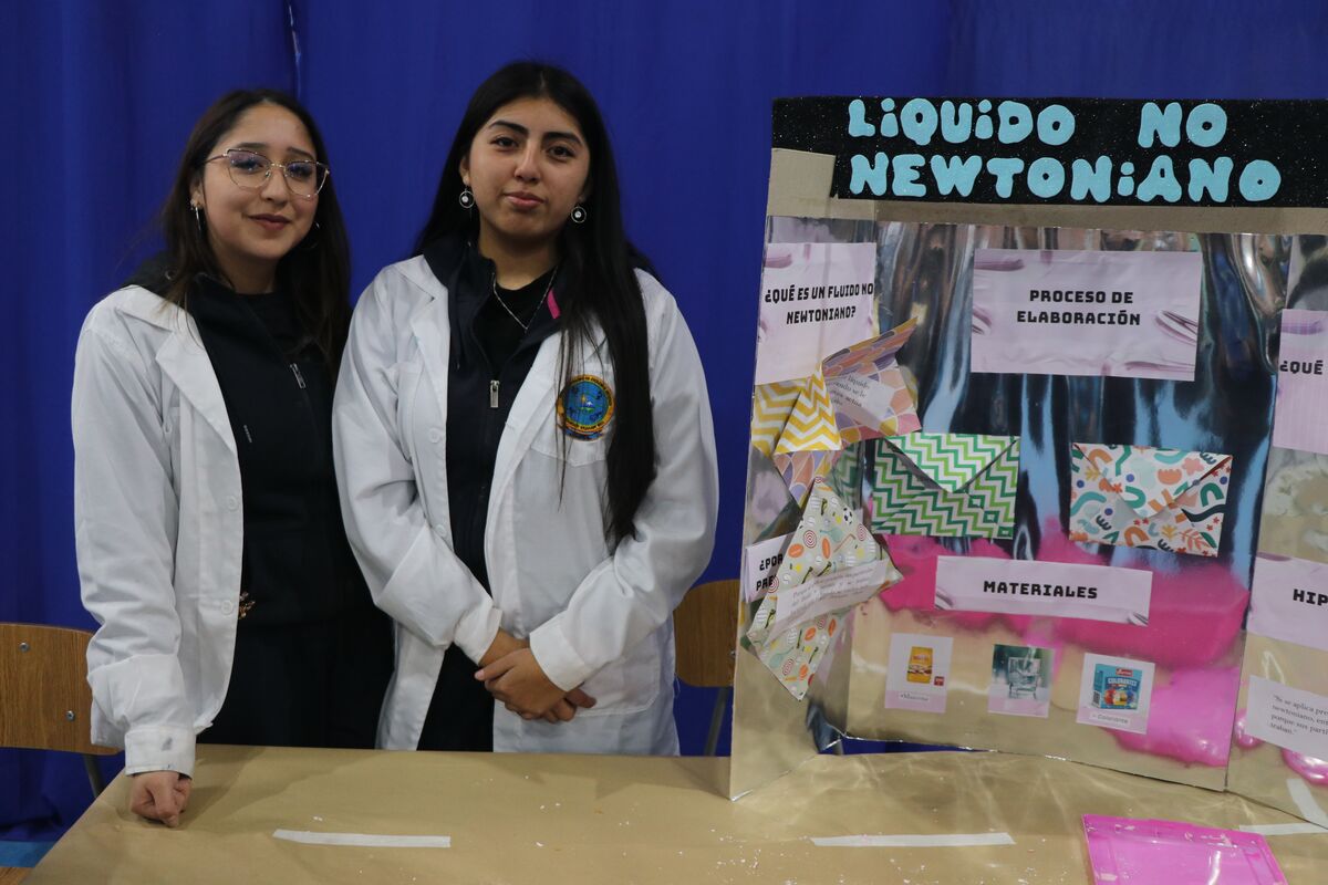 Estudiantes con delantal de laboratorio presentando su maqueta